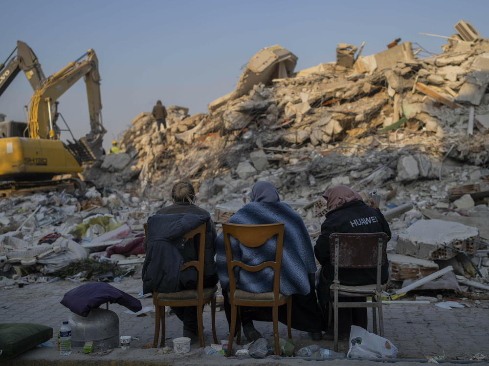 Women sit in front of the rubble of an area destroyed during the earthquake in Antakya, southeastern Turkey, Sunday, Feb. 12, 2023.