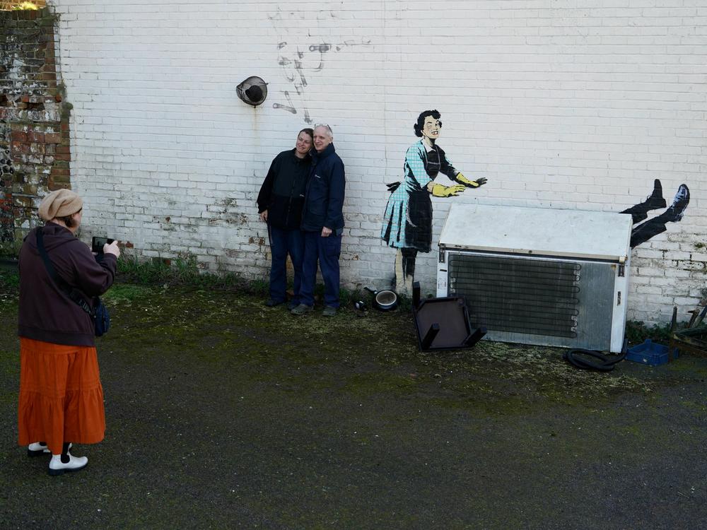 People gathered to see a Banksy artwork on the side of a house in Margate, England, on Valentine's Day. The work depicts a 1950s housewife with a swollen eye, missing a tooth — and apparently shutting a man in a freezer. The freezer was later removed by council workers.