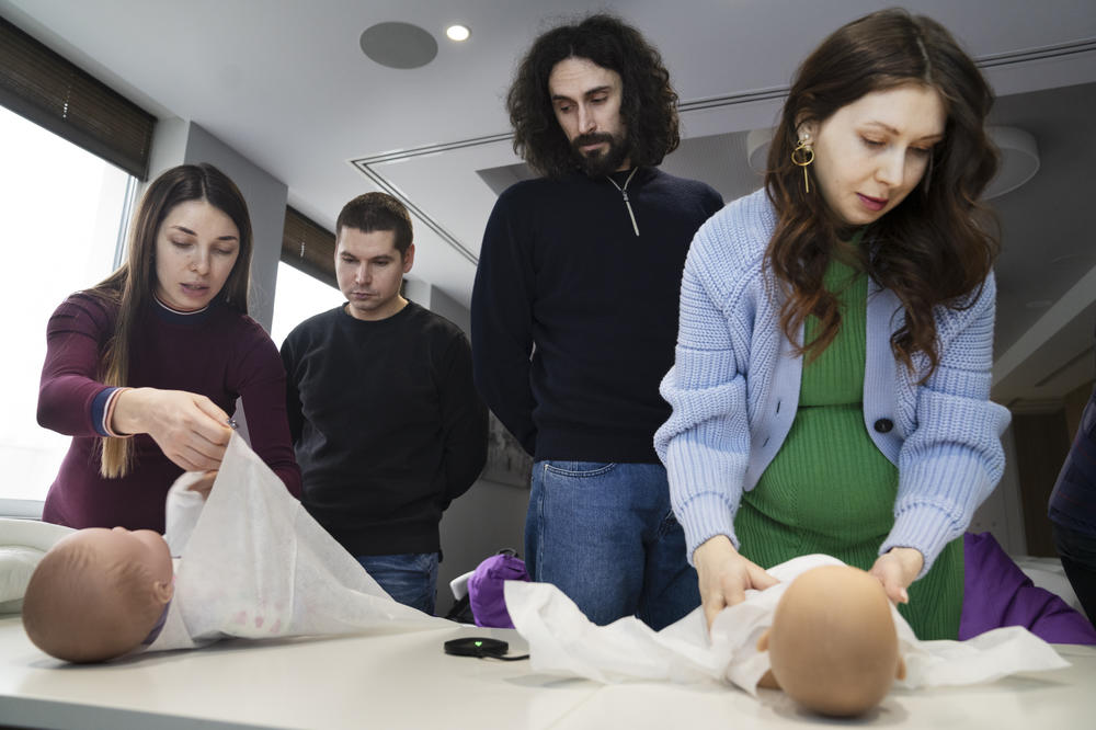 Expecting couples practice swaddling plastic babies at a class for new parents.