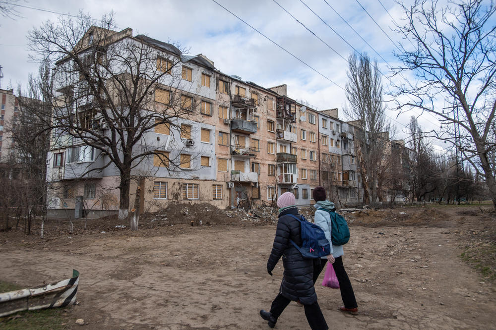 Two women walk past a building damaged by a strike in Kherson, Ukraine.
