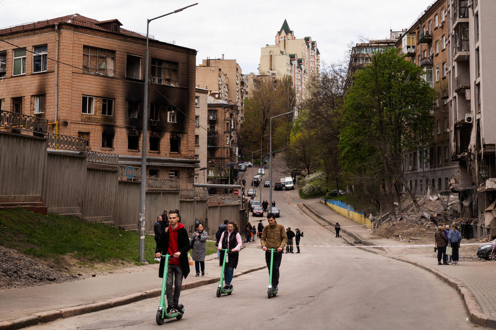 People ride scooters in Kyiv in April, looking at buildings that were damaged by a Russian missile strike the previous week.