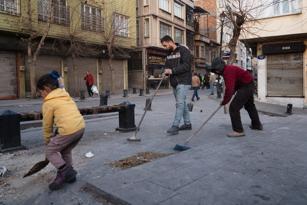 Yusuf Nahsen (center) sweeps the ground with a couple of kids in the area around where the tents are set up in Gaziantep.