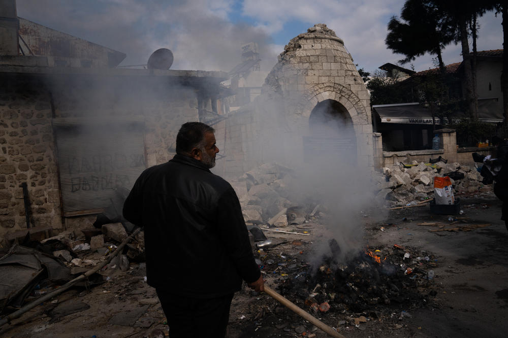 A man shovels trash into a fire on the street in front of where the minaret of Sermaye Mosque stood before the earthquake caused it to fall.