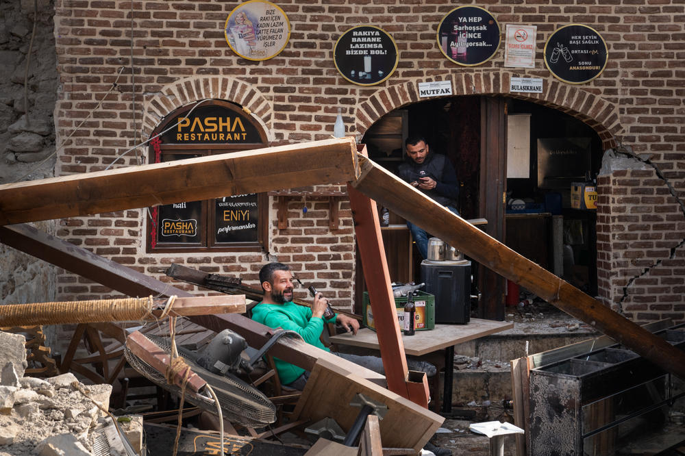 Orhan Uyanik (left), the owner of Pasha Restaurant in Antakya, sits in the rubble and opens one of the remaining beers that survived the quake.