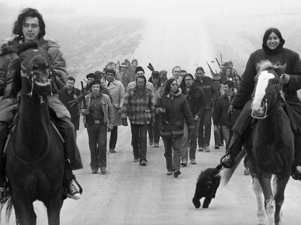 Assistant U.S. Attorney General Harlington Wood, third row center without hat, is escorted into the village of Wounded Knee by Russell Means (second row, left) and other members of the American Indian Movement on March 13, 1973.