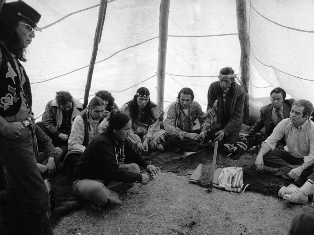 Assistant U.S. Attorney General Kent Frizzell, right, meets with AIM leaders at Wounded Knee in April 1973. Kneeling is Wallace Black Elk and to his left are AIM leaders Russell Means, Dennis Banks and Carter Camp.