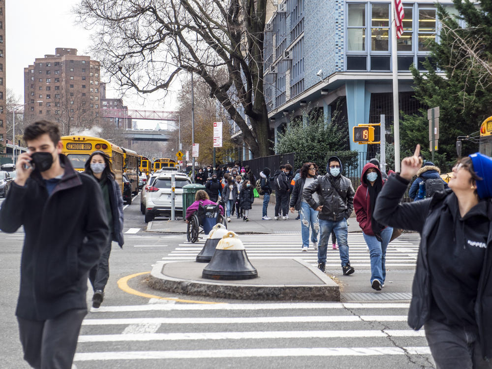 Pedestrians cross Houston Street as students wearing masks leave the New Explorations into Science, Technology and Math (NEST+m) school in the Lower East Side neighborhood of Manhattan on Tuesday, Dec. 21, 2021, in New York.