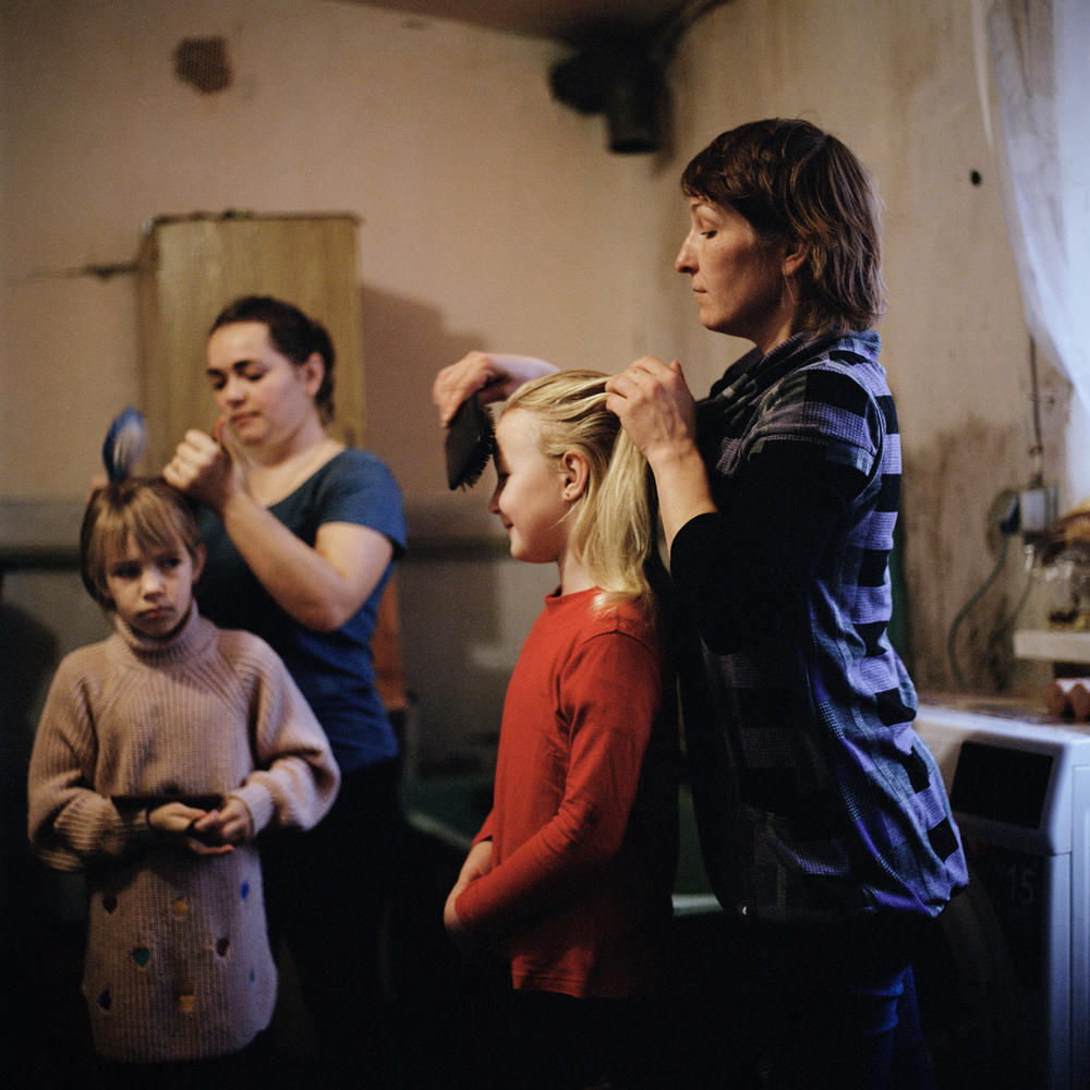 Olga Grinik (right) combing Miroslava's hair and Hanna Drobysh (left) combing her daughter Angelina's hair in their kitchen in Poltava region. December 2022.