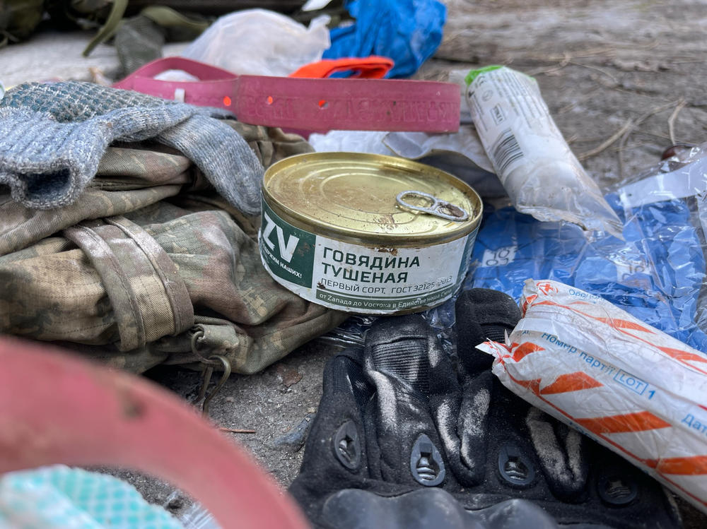 The contents of backpacks carried by Russian soldiers who were killed in a trench by Ukrainian soldiers. In the foreground is a tin of Russian beef. Behind it sits a flimsy, pink rubber tourniquet.