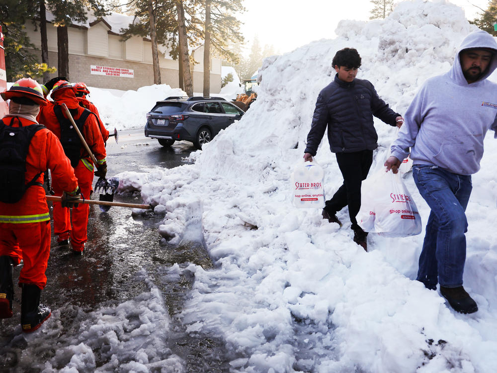 A crew of inmate firefighters walk back to their vehicle after shoveling and clearing snow, while people carry bags of food on Friday. A series of winter storms in the San Bernardino Mountains in Southern California left residents stranded due to the snowfall.