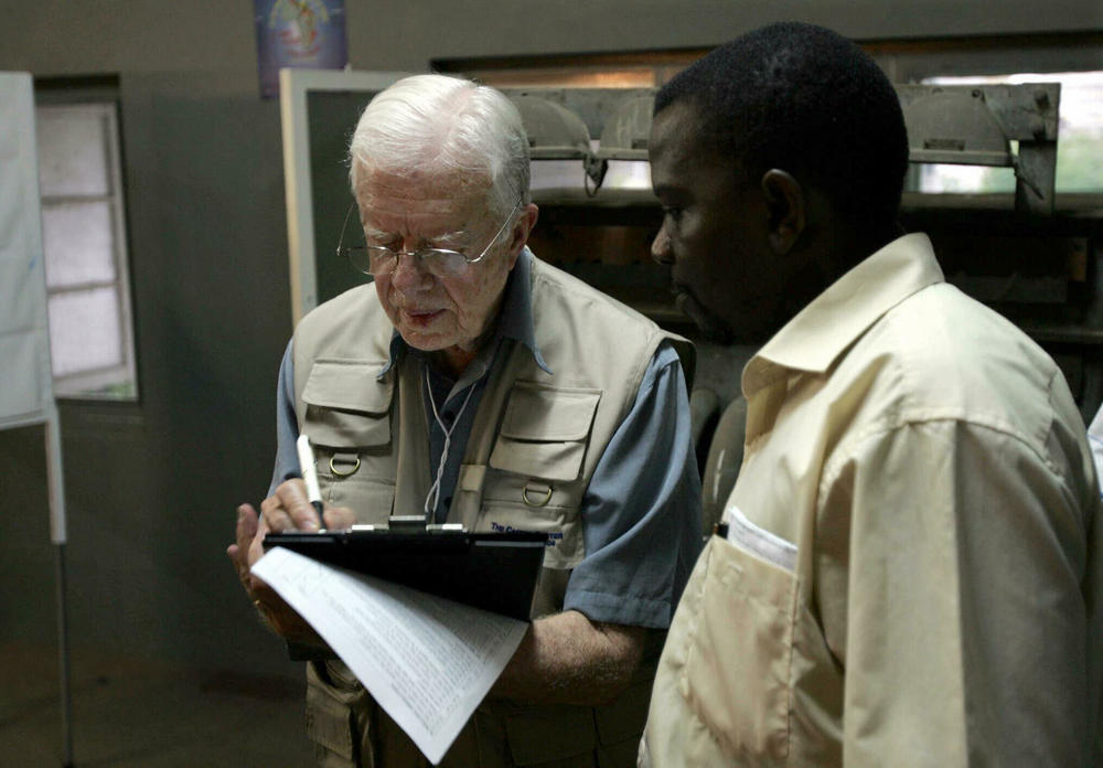 December 2, 2004: Former U.S. President Jimmy Carter (L) takes notes while listening to a translater during his polling station observation visit in Maputo, Mozambique. Mozambique's long-time President Joaquim Chissano expressed surprise at the abysmal turn-out in elections to choose his successor, and blamed the poor showing on widespread illiteracy and ignorance of political systems.