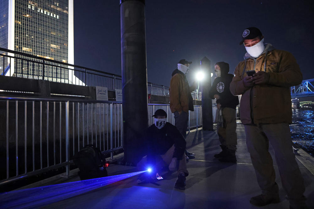 Members of the white nationalist group National Socialist Florida, including the group's leader Josh Nunes, right, use a laser projector to display white nationalist and anti-LGBTQ images on the sides of high-rise buildings in Jacksonville, Florida.