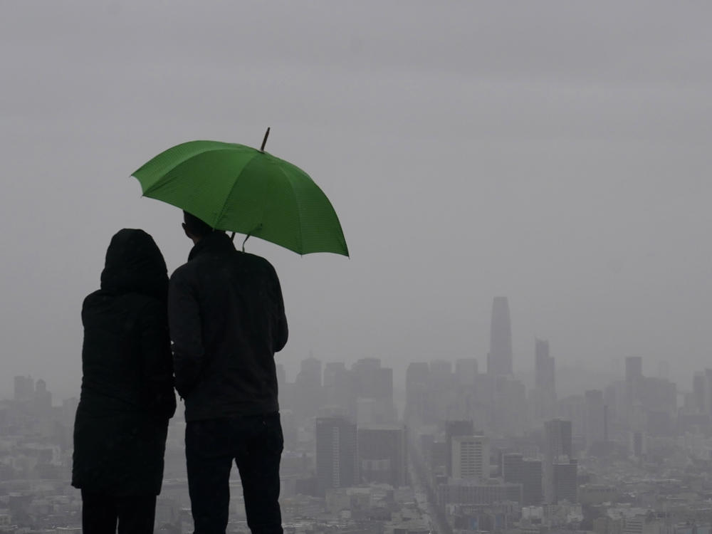 People stand under an umbrella while looking toward the skyline from Twin Peaks in San Francisco, Thursday, March 9, 2023.