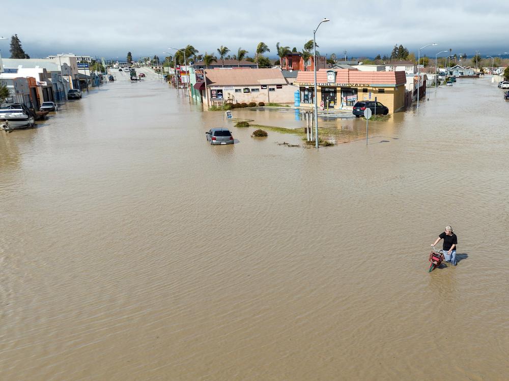 An aerial view shows a man navigating floodwaters with his bicycle in the unincorporated community of Pajaro in California on March 11. Residents were forced to evacuate in the middle of the night after an atmospheric river surge broke the Pajaro Levee and sent flood waters flowing into the community.