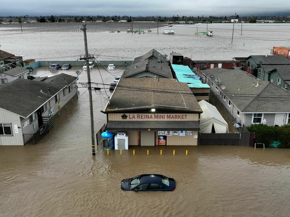 This aerial photograph shows a car and market shop in floodwaters in Pajaro, Calif., on Saturday. More rain and snow is expected in the state this week.