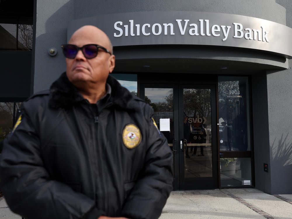 A security guard at Silicon Valley Bank monitors a line of people outside the office in Santa Clara, Calif., on March 13, 2023. The Fed will now need to factor in the impact of the collapse of the lender, along with Signature Bank, as it makes its next decision on interest rates.