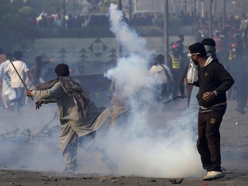 A supporter of former Prime Minister Imran Khan hurls back a tear gas shell fired by riot police officers to disperse them during clashes, in Lahore, Pakistan, Wednesday, March 15, 2023.