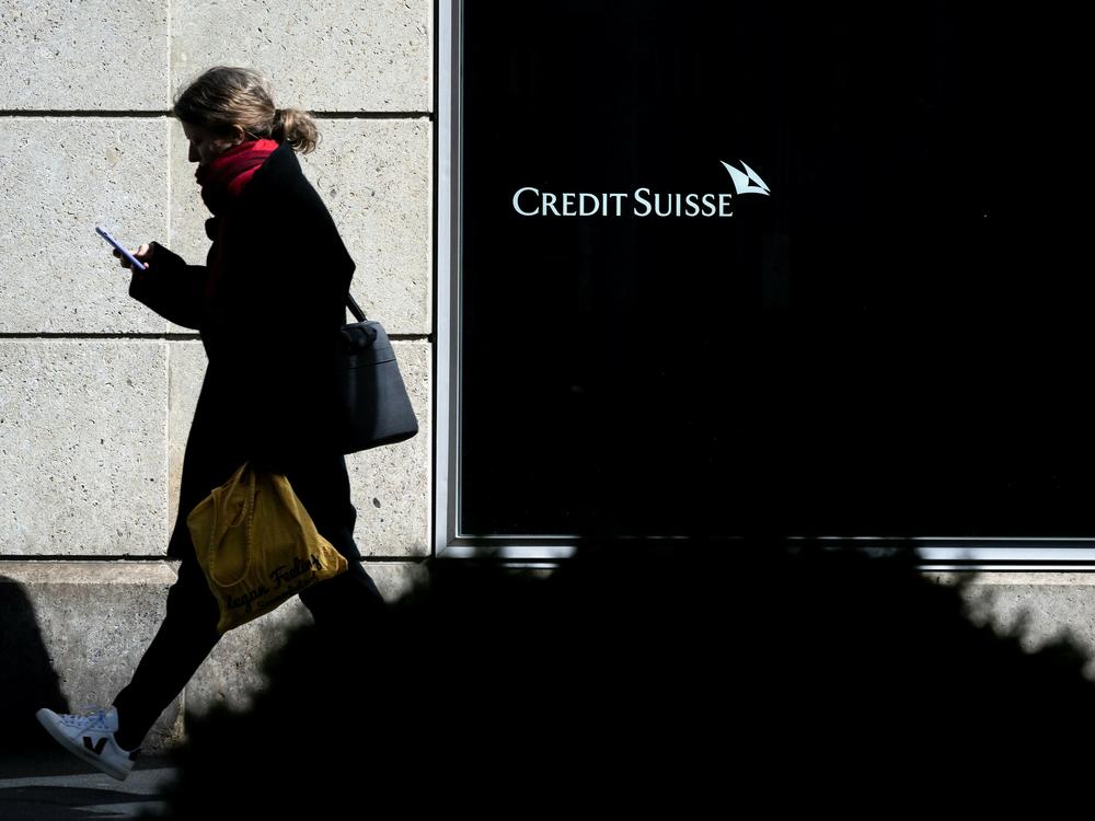 A woman is seen in silhouette walking past a branch of Switzerland's Credit Suisse bank in western Switzerland, on March 15, 2023. A steep drop in shares of the troubled lender have sparked fears that fears about the banking system are spreading globally.