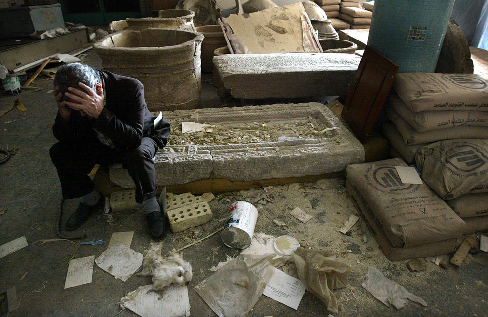 April 13, 2003: Iraqi National Museum Deputy Director Mushin Hasan holds his head in his hands as he sits on destroyed artifacts in Bagdhad, Iraq. The museum was severely looted.