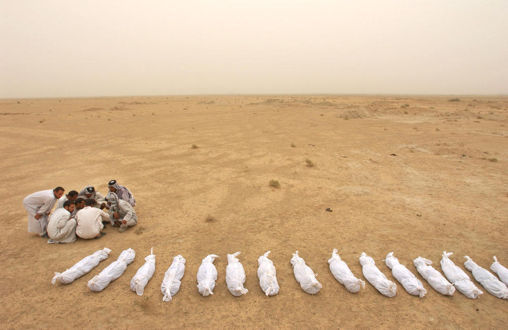 May 31, 2003: Iraqi men check a list as sheets containing the remains of bodies excavated from a mass grave lie in the desert on the outskirts of Musayib, approximately 30 miles south of Baghdad. Locals said the mass grave contained the remains of hundreds of Shia Muslims allegedly executed by Saddam Hussein's regime after their uprising following the 1991 Gulf War.