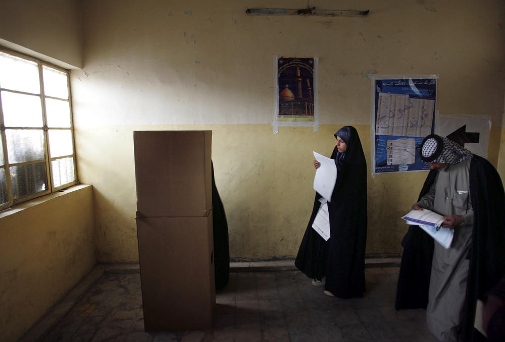 Jan. 30, 2005: Voters look over their ballots before voting behind a cardboard screen on Election Day in Baghdad's Sadr City neighborhood.
