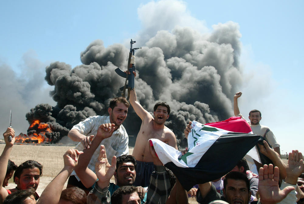 April 9, 2004: Iraqi insurgents wave their national flag as they celebrate in front of a burning U.S. military tanker after attacking it in Abu Gharib.