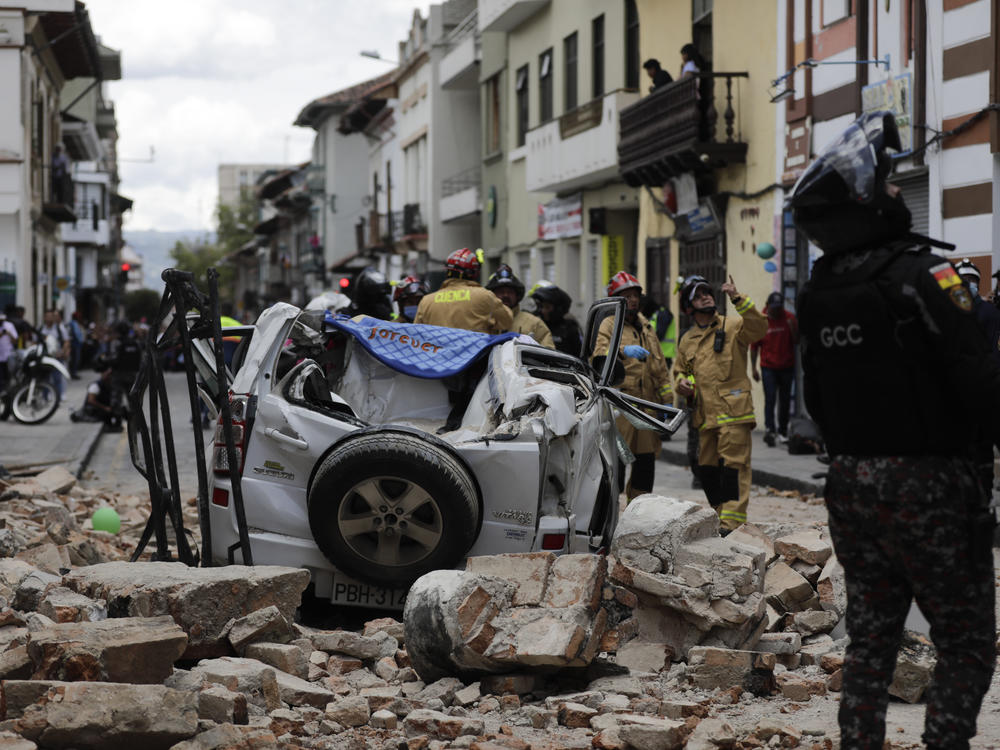 A police officer looks up next to a car crushed by debris after an earthquake shook Cuenca, Ecuador, on Saturday.