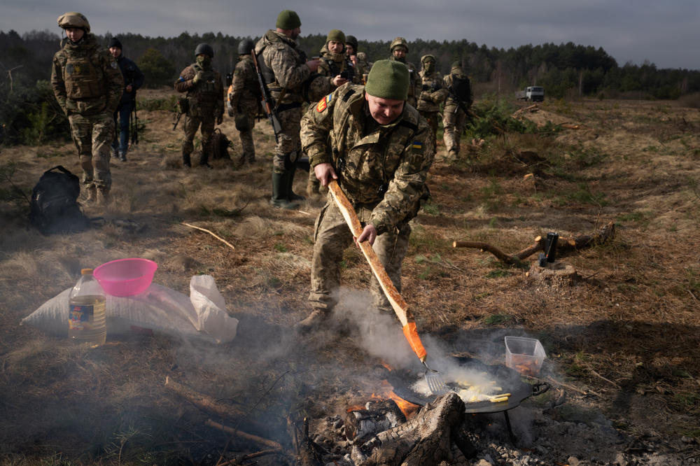 A soldier fries potatoes over a fire.