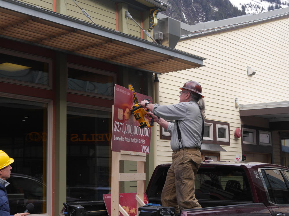 Bob Schroeder, an organizer with 350Juneau, sawed credit card replicas in half outside a Wells Fargo branch in Juneau, Alaska.
