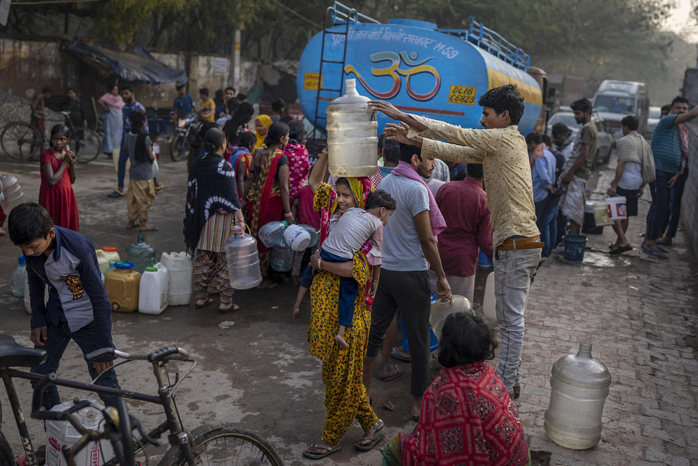A woman balances a water can on her head while people collect water from a mobile water tanker in a residential area in New Delhi, India.