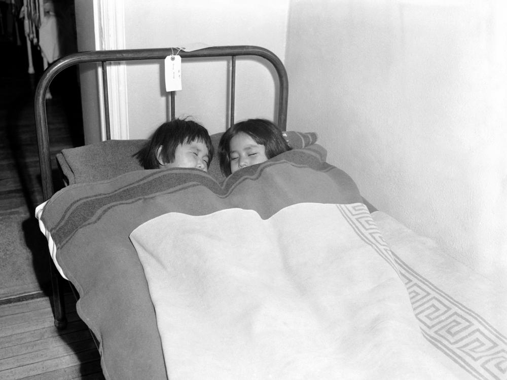 Two girls are seen sharing a bed due to overcrowding at a Navajo boarding school in Chinle, Az., in Dec. 1945.
