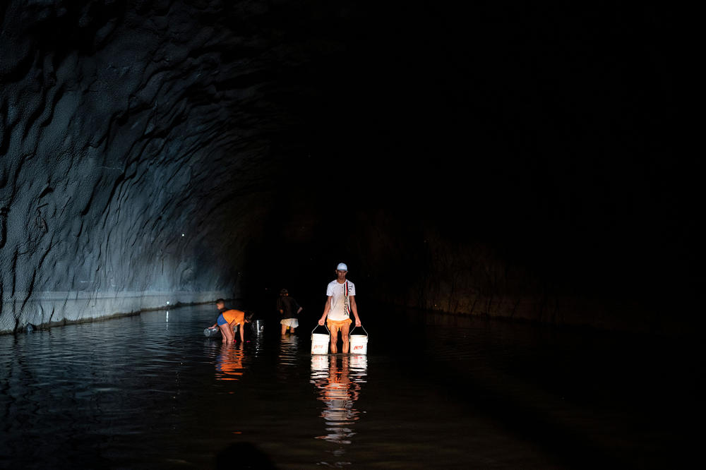 Residents of the El Cardon community, who do not receive drinking water at home, carry buckets and drums with water collected from a natural pond formed in a tunnel in Caracas, Venezuela.