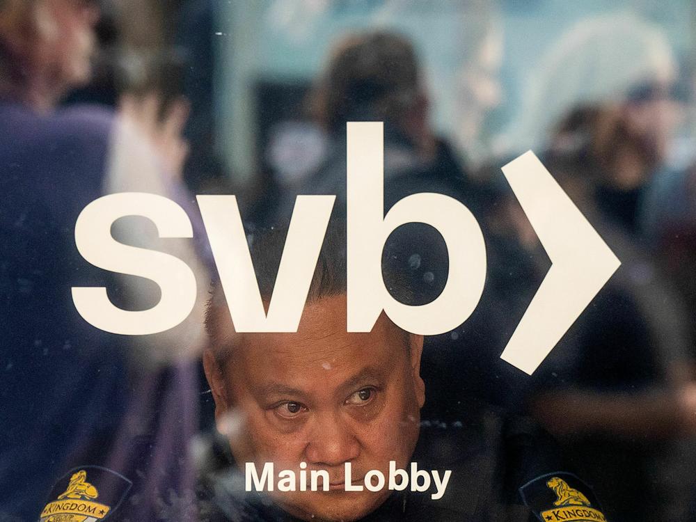 A security guard looks out a door as customers line up at Silicon Valley Bank headquarters in Santa Clara, California on March 13, 2023.