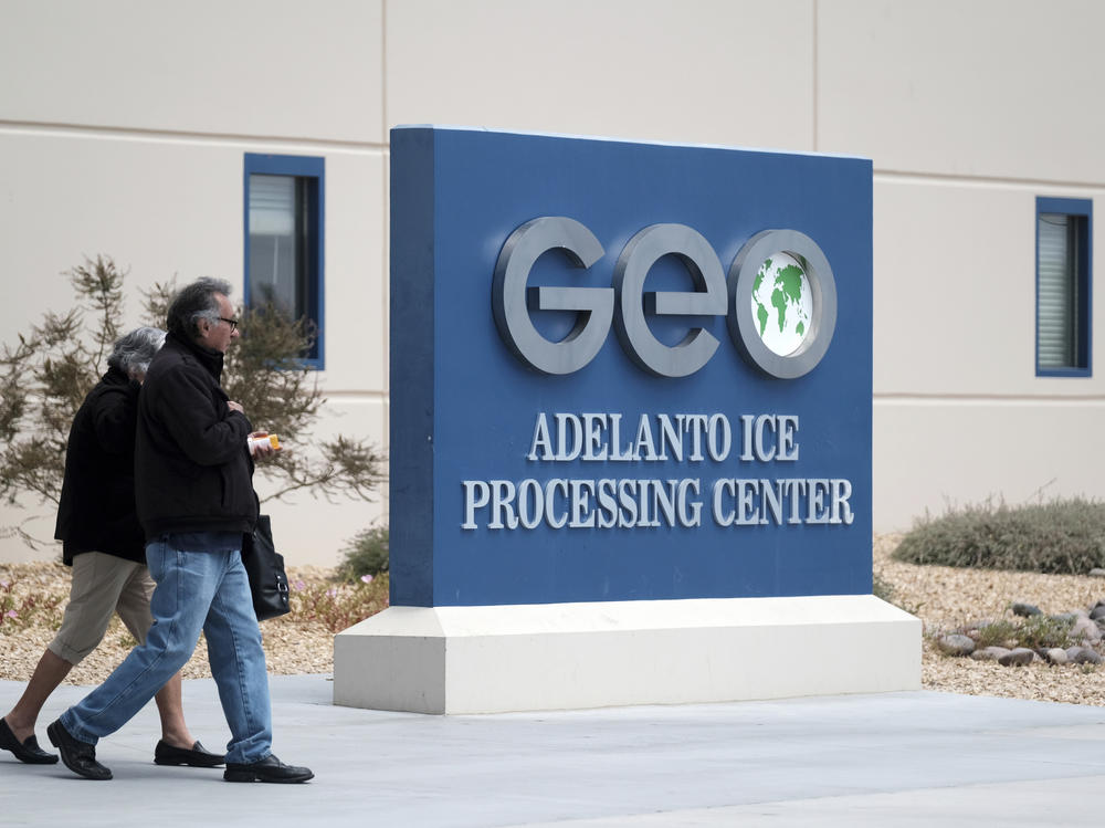People walk outside the U.S. Immigration and Enforcement Processing Center operated by GEO Group Inc. in Adelanto, Calif. The company is facing a lawsuit for the alleged use of hazardous chemicals in the facility during the COVID-19 pandemic.
