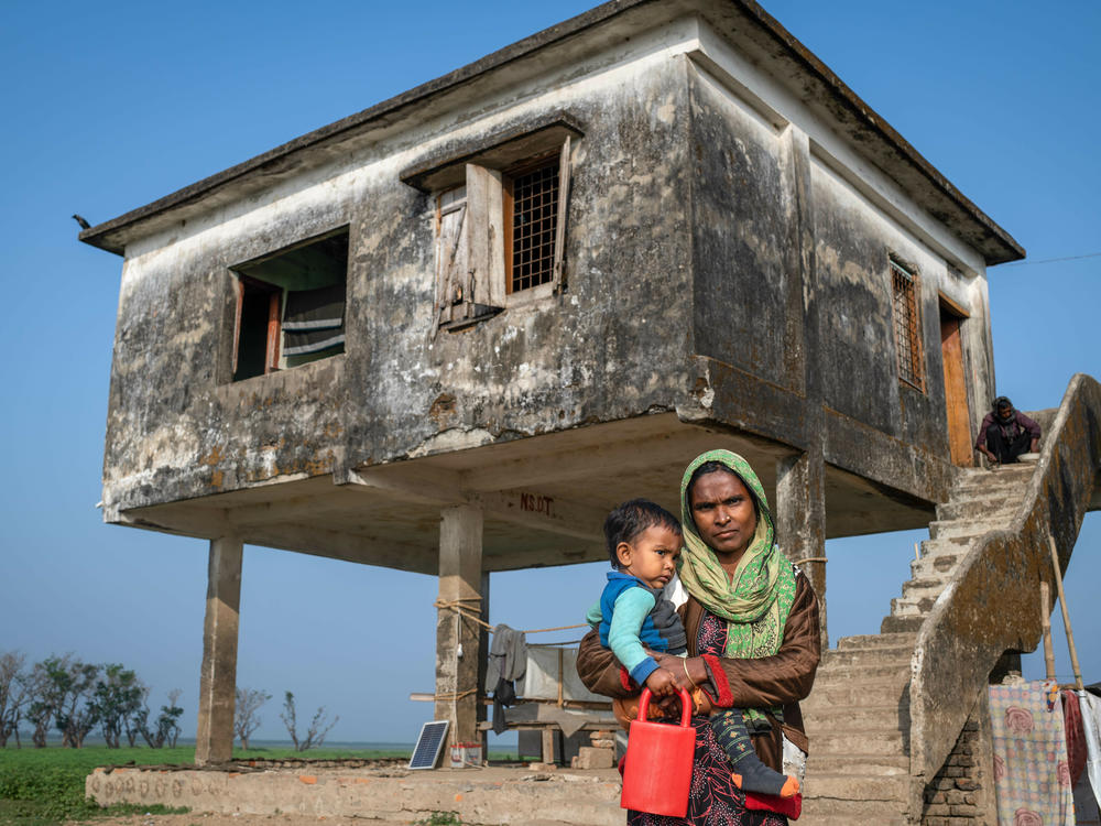 Kelna Begum, 30, stands with her child in front of a building that's been raised to survive seasonal floods in her village of Golabari in the Sunamganj region of northern Bangladesh.