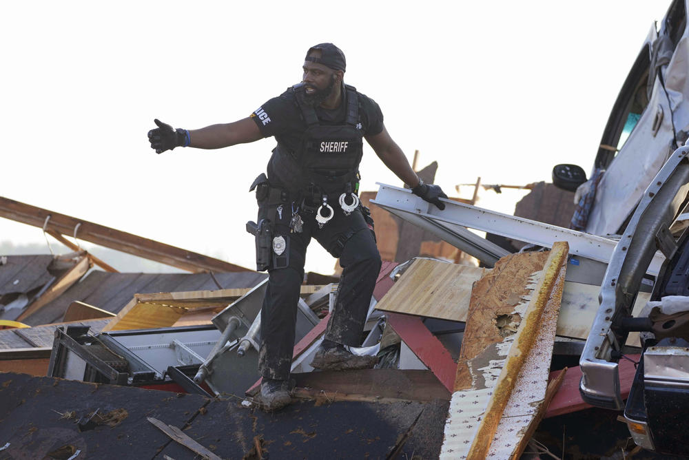 A sheriff's deputy gives the all-clear signal after climbing onto a piled up vehicle to search for survivors or the deceased at Chuck's Dairy Bar in Rolling Fork, Miss.