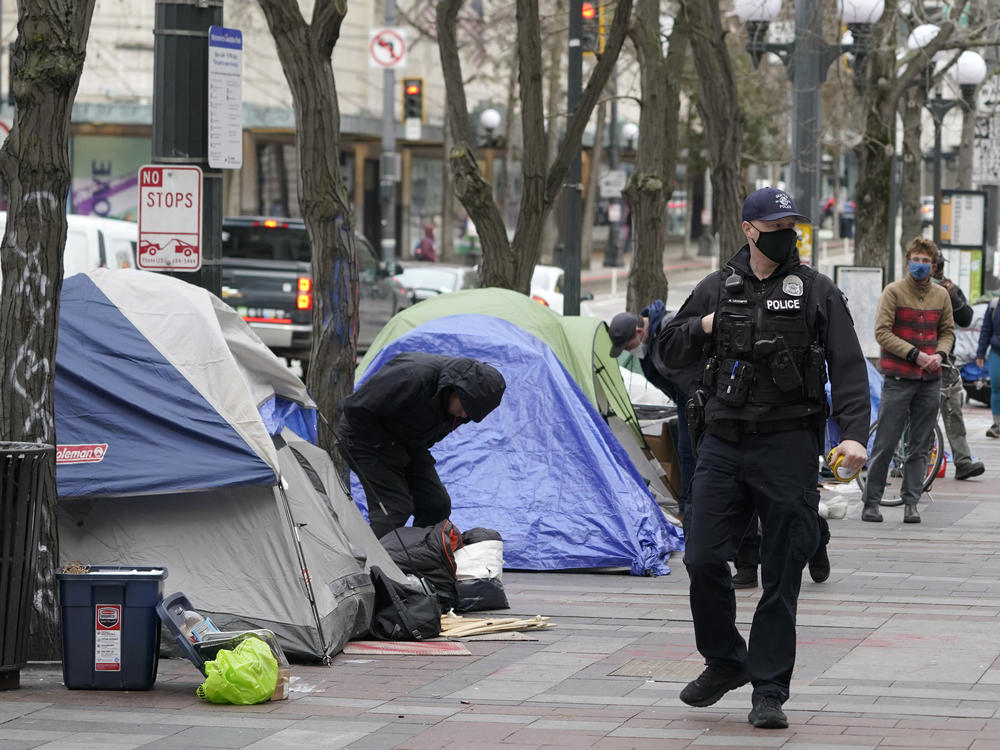 A Seattle police officer walks past tents used by people experiencing homelessness, March 11, 2022, during the clearing and removal an encampment in Westlake Park in downtown Seattle.