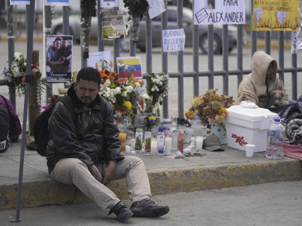 A Venezuelan migrant sits on the sidewalk where an altar was created with candles and photos outside the Mexican immigration processing center that was the site of a deadly fire, as migrants wake up after spending the night on the sidewalk in Ciudad Juárez, Mexico, on Thursday.