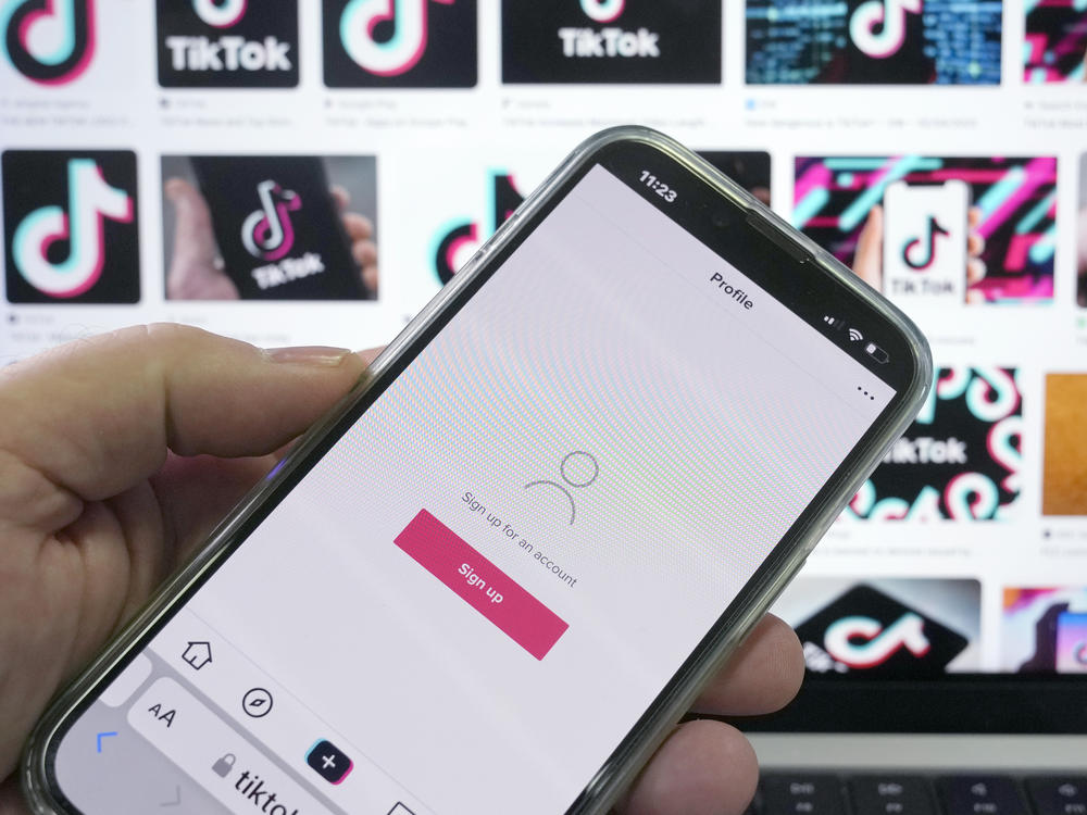 A sign up page for the application TikTok is shown on a cell phone in front of a screen with logos for the company in Sydney, Tuesday, April 4, 2023.
