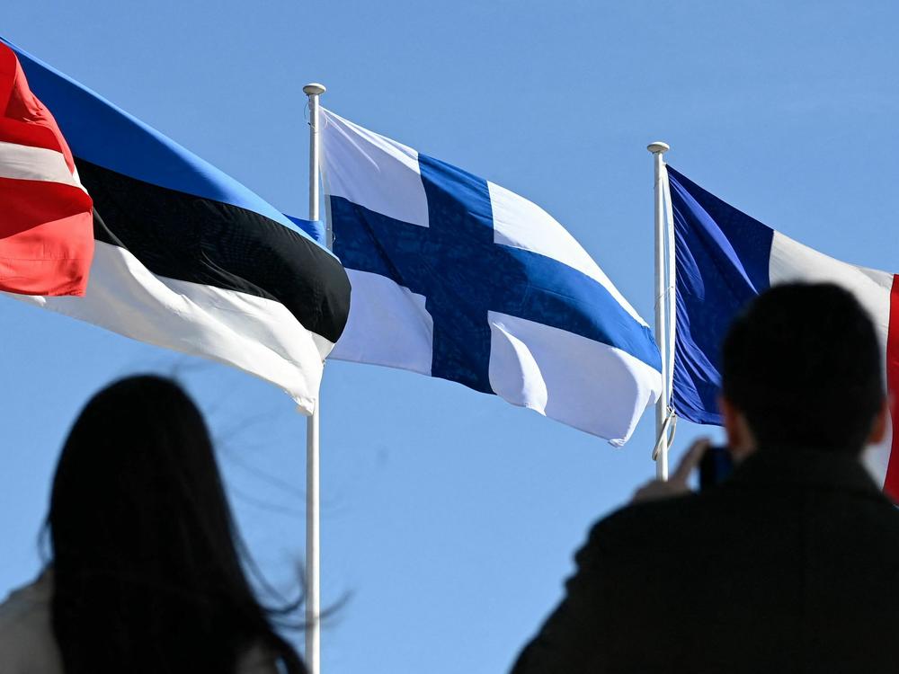 People stand in front of the Finnish national flag after a flag-raising ceremony at the NATO headquarters in Brussels on April 4, 2023.