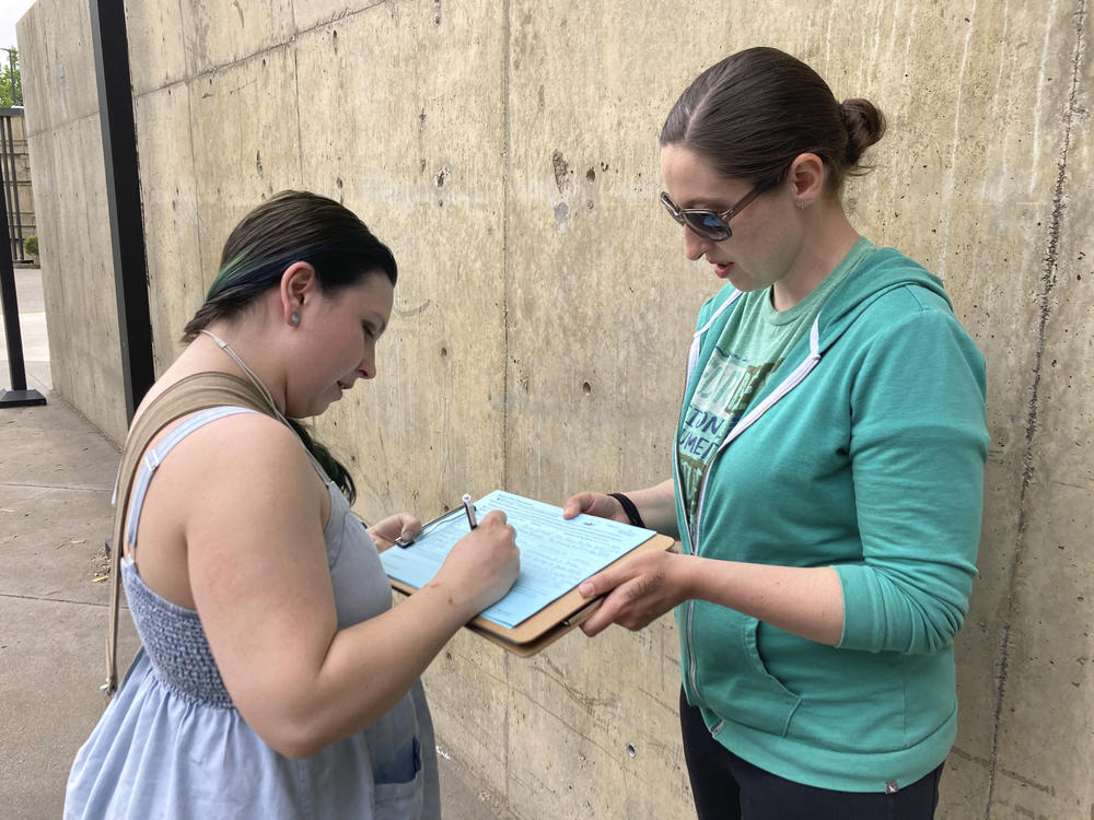 A resident signs an initiative petition supporting a gun safety ballot measure on June 7, 2022, outside a library in Salem, Ore., as a signature gatherer holds the clipboard.