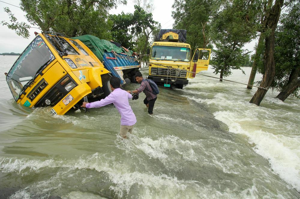 People wade past stranded trucks on a flooded street in Bangladesh. Experts say climate change is increasing the frequency, ferocity and unpredictability of floods.