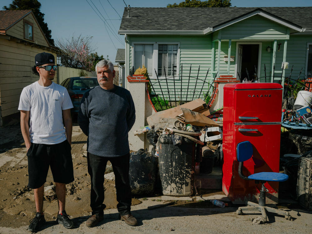 Armando Alvarado, 22, and his father Jesús Valtierra, 52, stand outside their home in Pajaro, California on March 24, 2023. Alvarado worries about how costs to repair the damage will affect his family's rent in a place where a one-bedroom apartment can cost as much as $2,800.
