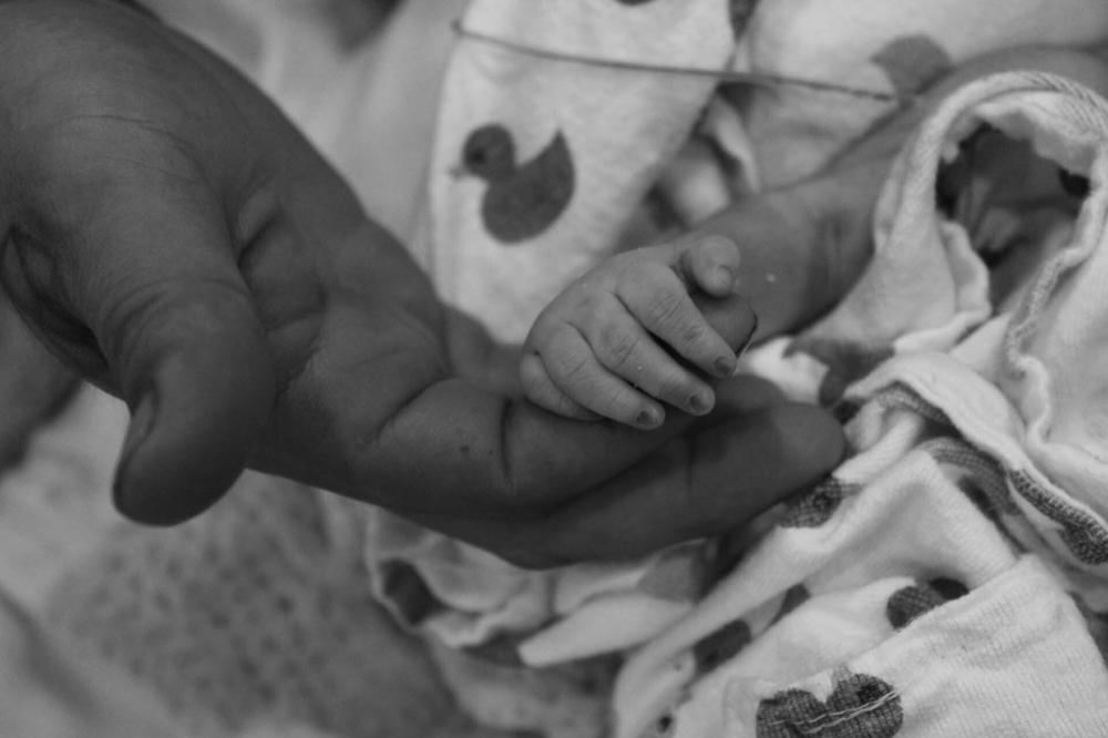 Luis Villasana holds the hand of their baby, who lived for only four hours.