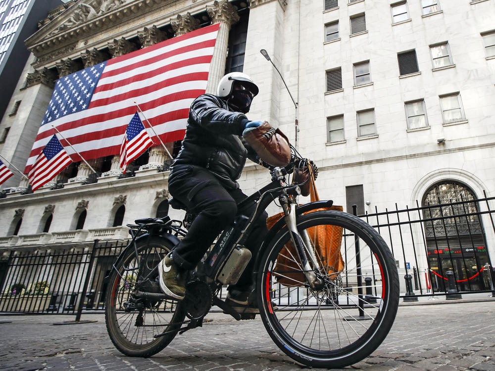 A delivery worker rides his electric bicycle past the New York Stock Exchange on March 16, 2020, in New York. Electric bicycles and scooters are being blamed in an increasing number of fires resulting in injuries and deaths in New York City.