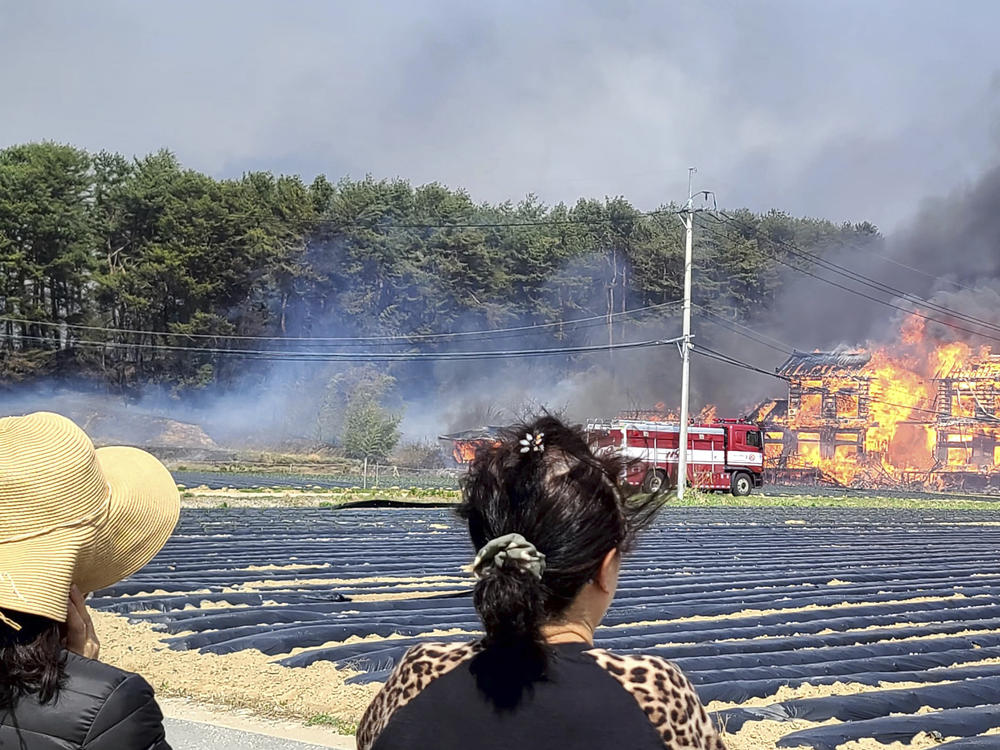 People look at a fire as firefighters work to extinguish in Gangneung, South Korea, Tuesday, April 11, 2023.