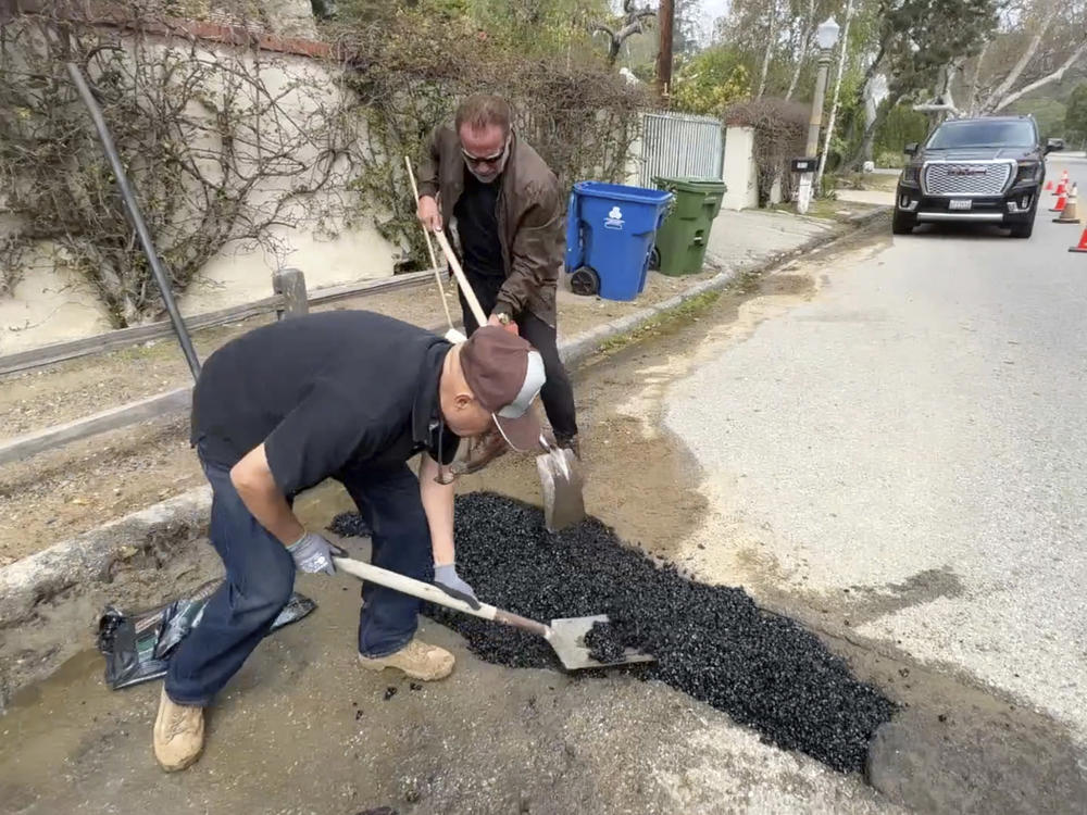 This video still image provided by Arnold Schwarzenegger's office, shows the former California governor (center back) repairing a pothole on a street in his Los Angeles neighborhood on Tuesday.