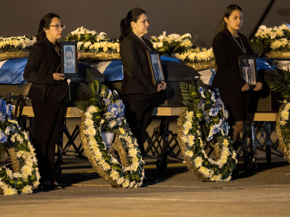 Foreign Ministry officers hold portraits beside the coffins of Guatemalan migrants whose remains arrived at the La Aurora Air Force Base in Guatemala City on Tuesday. The Mexican Air Force transported the bodies of 17 migrants who died in a fire at an immigration detention center in Ciudad Juárez, Mexico.