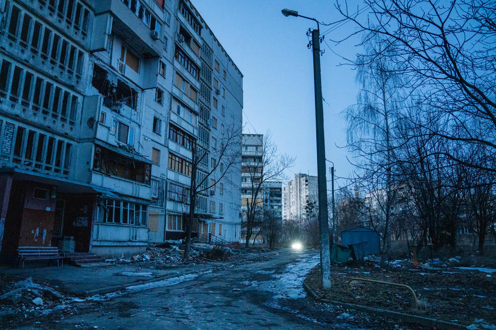 A car's headlights can be seen down a street next to some apartment buildings in Saltivka just after sunset.