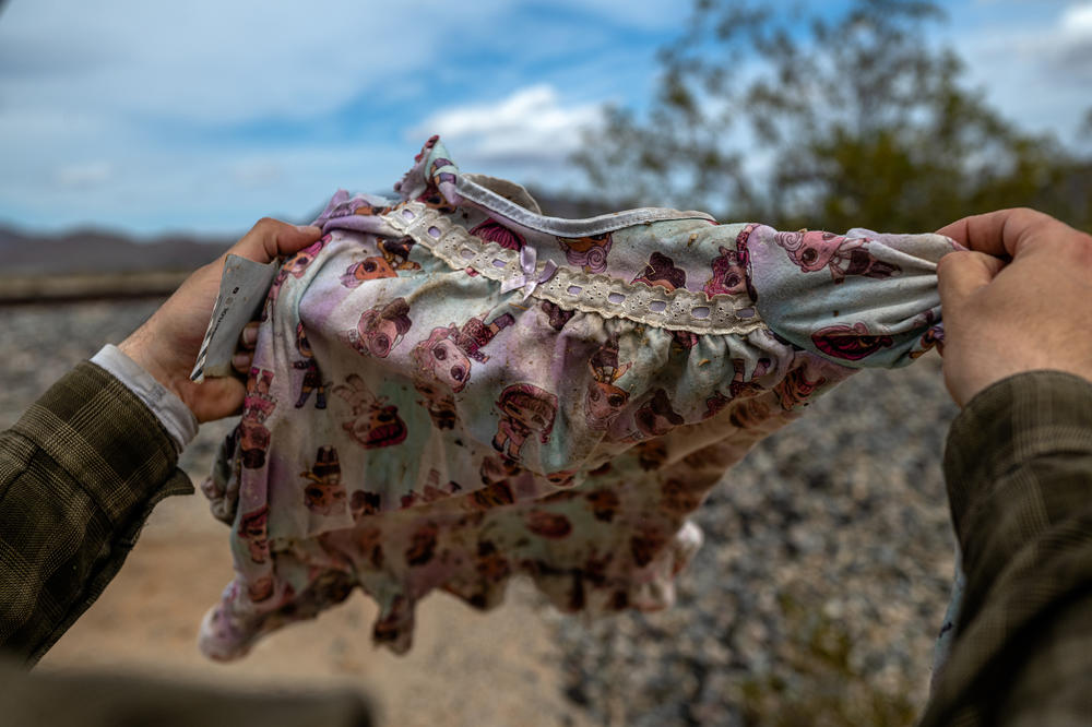 James Cordero examines some children's clothes he found in a bush near a bridge. Discarded items are found throughout the desert.